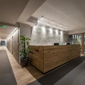 Moderne Hotellobby mit Holzrezeption, Steinwand, Flur und Glastür Eingang