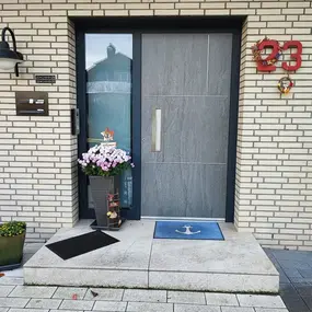 Moderner Hauseingang mit grauer Tür, Blumen, Fußmatte und Hausnummer 23
