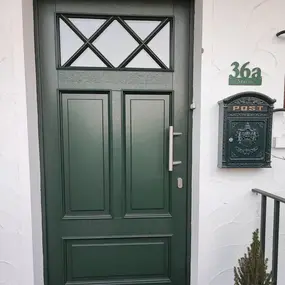 Grüne Haustür mit Glaseinsatz, Briefkasten und Hausnummer an Fassade