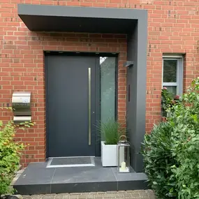 Moderne Haustür in Anthrazit mit Vordach, Backsteinfassade und Pflanzen﻿