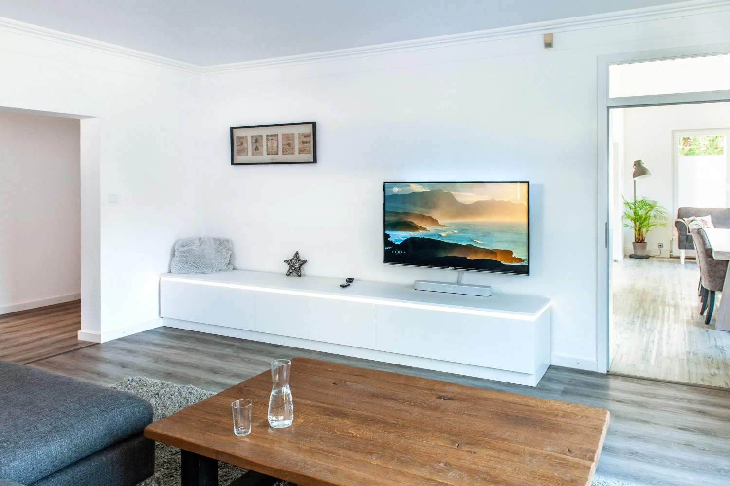 Modernes Wohnzimmer mit TV auf Lowboard, Couchtisch und Durchgang zum Esszimmer