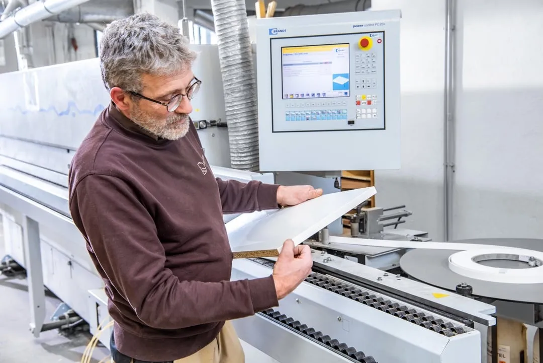 Mitarbeiter prüft Holzplatte an CNC-Kantenanleimmaschine in Schreinerei